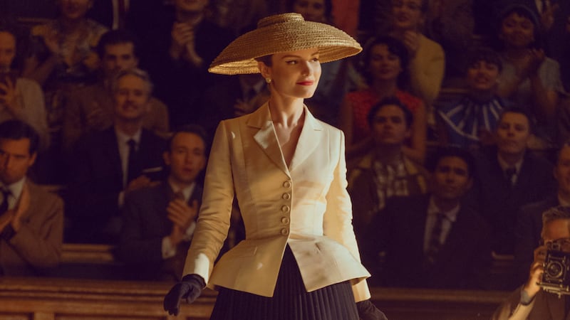 A smiling model wearing Dior's famous bar jacket walks the runway.